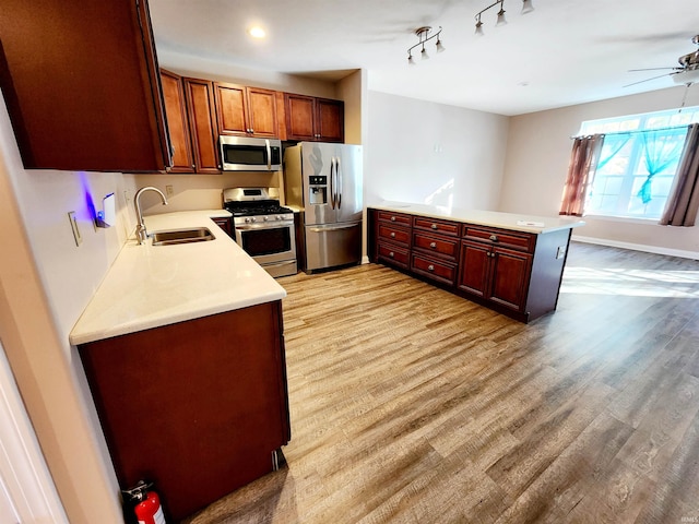 kitchen featuring appliances with stainless steel finishes, sink, kitchen peninsula, light hardwood / wood-style floors, and ceiling fan