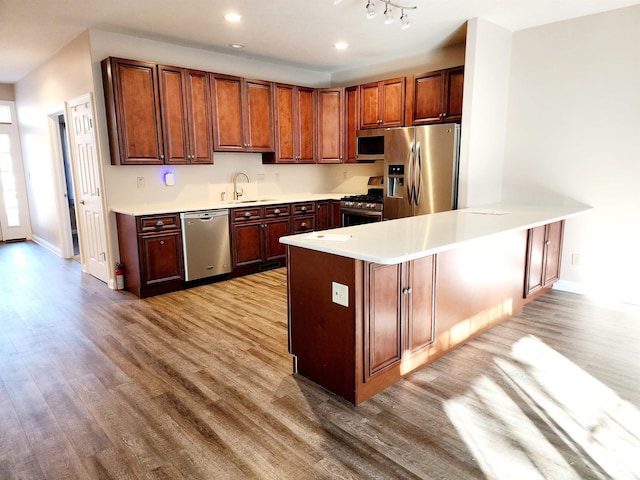 kitchen with sink, kitchen peninsula, stainless steel appliances, and light wood-type flooring