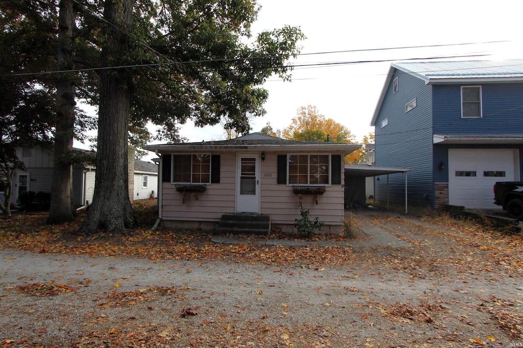 view of front of property featuring entry steps, dirt driveway, a garage, and a carport