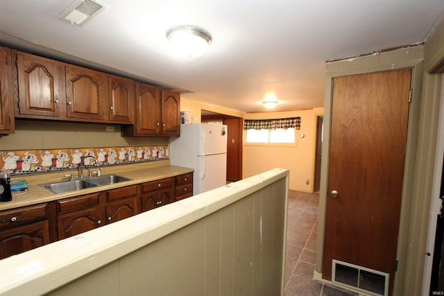 kitchen with dark tile patterned flooring, sink, white refrigerator, and decorative backsplash