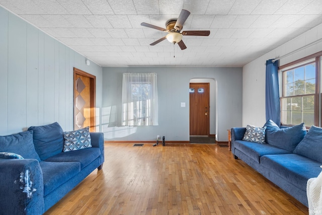 living room featuring ceiling fan, wood walls, and light wood-type flooring