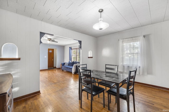 dining room with hardwood / wood-style flooring, wooden walls, and ceiling fan