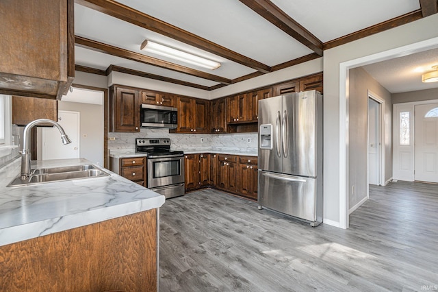 kitchen with decorative backsplash, ornamental molding, sink, appliances with stainless steel finishes, and light hardwood / wood-style floors