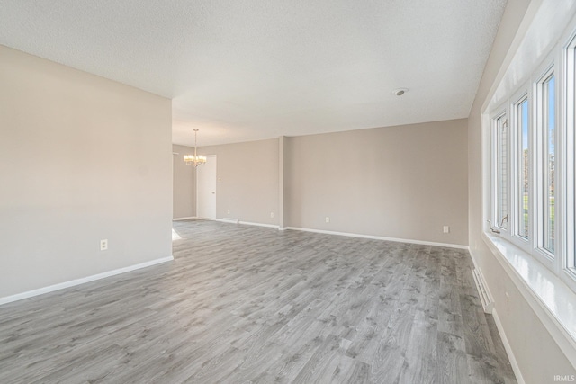 unfurnished room with a notable chandelier, a textured ceiling, and light wood-type flooring