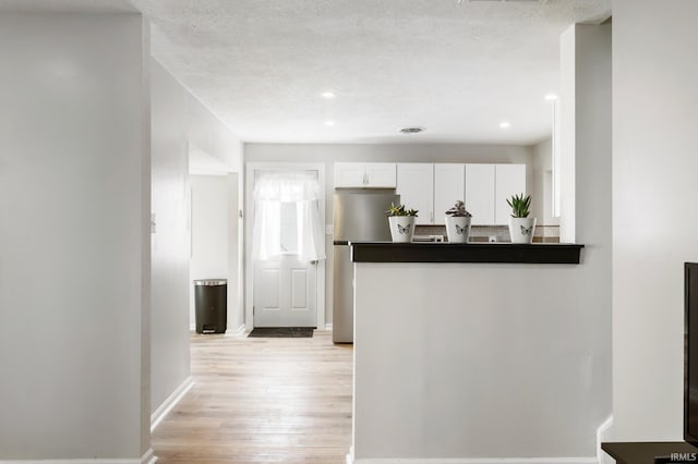 kitchen with a textured ceiling, stainless steel refrigerator, light hardwood / wood-style flooring, and white cabinets