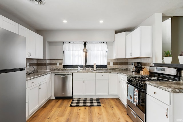 kitchen with decorative backsplash, appliances with stainless steel finishes, white cabinets, and light hardwood / wood-style floors