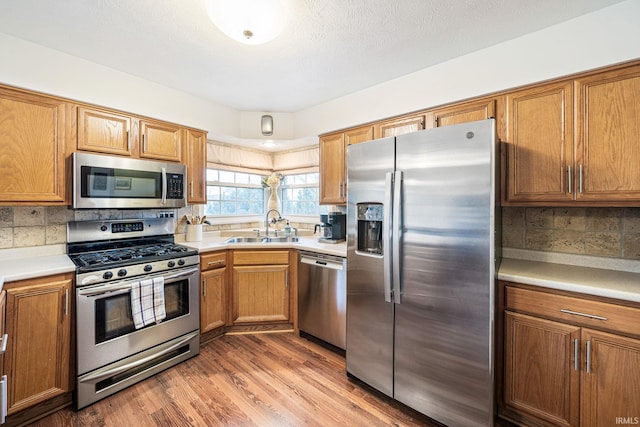 kitchen featuring appliances with stainless steel finishes, sink, light wood-type flooring, backsplash, and a textured ceiling