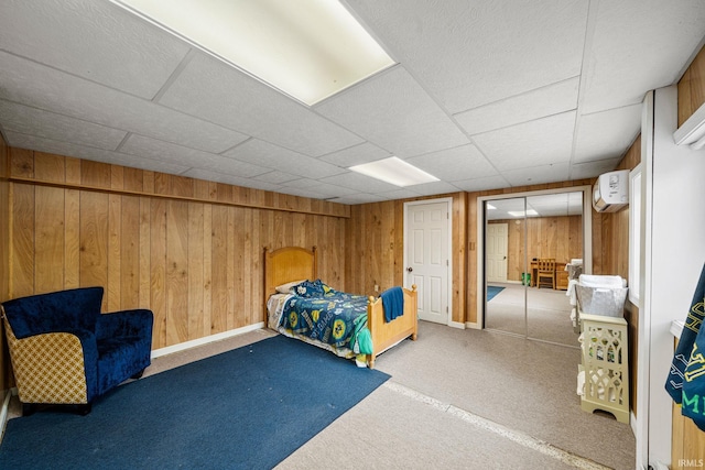 carpeted bedroom with a wall mounted air conditioner, wood walls, and a paneled ceiling