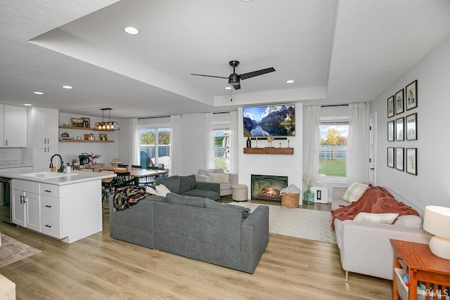 living room featuring ceiling fan, a raised ceiling, and light hardwood / wood-style flooring