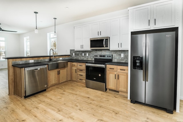 kitchen with dark countertops, appliances with stainless steel finishes, a sink, and light wood-type flooring