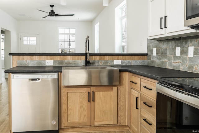 kitchen with decorative backsplash, a sink, dark countertops, a ceiling fan, and appliances with stainless steel finishes
