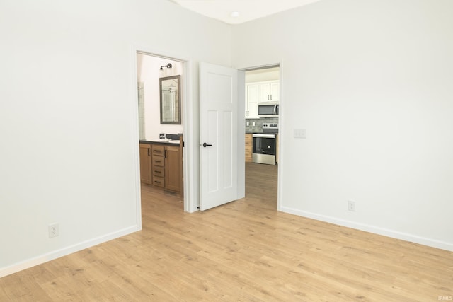 unfurnished bedroom featuring baseboards, connected bathroom, and light wood finished floors