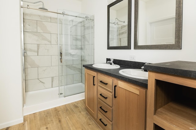full bathroom featuring double vanity, a sink, wood finished floors, and a shower stall