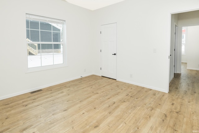 empty room featuring a healthy amount of sunlight, baseboards, light wood-style flooring, and visible vents
