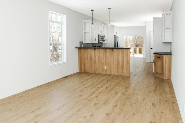 kitchen with open shelves, dark countertops, light wood-style flooring, stainless steel appliances, and a peninsula