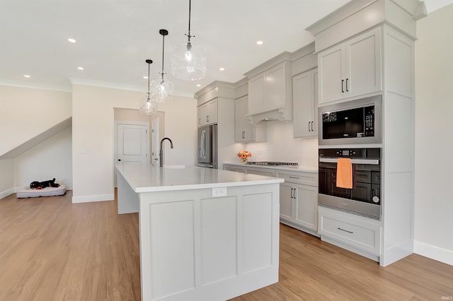 kitchen featuring light wood-type flooring, decorative light fixtures, an island with sink, and stainless steel fridge