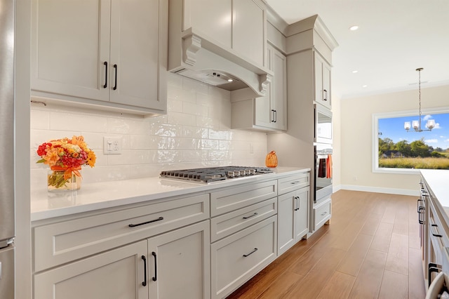 kitchen with light hardwood / wood-style flooring, decorative light fixtures, an inviting chandelier, premium range hood, and tasteful backsplash