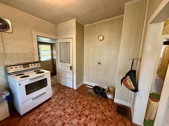 kitchen featuring white electric stove, wooden walls, and brick wall