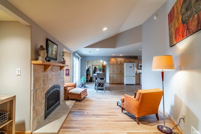 living room with vaulted ceiling, light hardwood / wood-style floors, and a tile fireplace