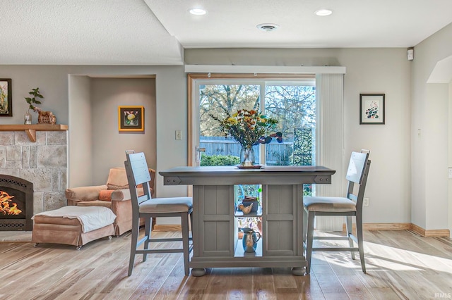 dining room featuring light hardwood / wood-style flooring, a textured ceiling, and a tiled fireplace