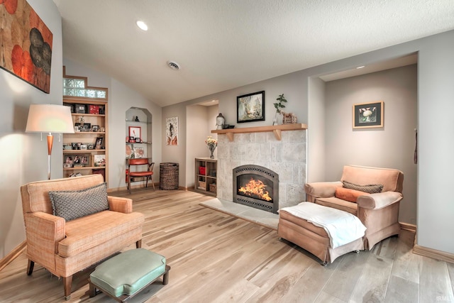 sitting room with vaulted ceiling, light wood-type flooring, and a tile fireplace