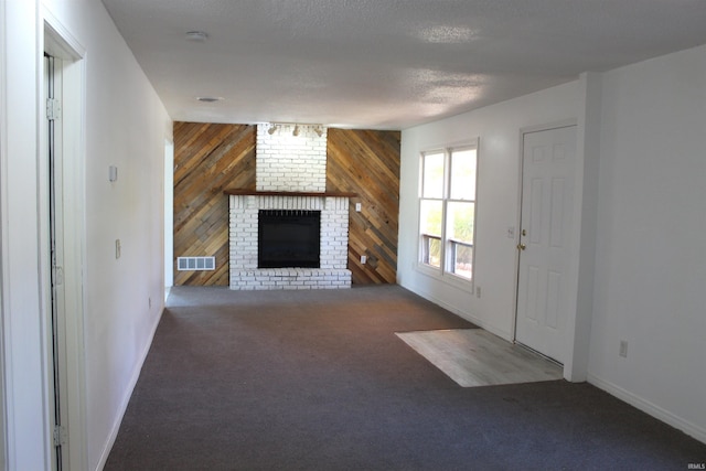 unfurnished living room with wood walls, dark colored carpet, a textured ceiling, and a brick fireplace