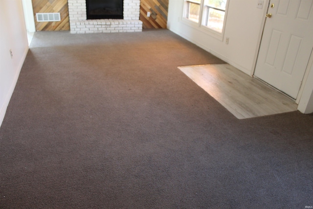 unfurnished living room with carpet, wooden walls, and a brick fireplace