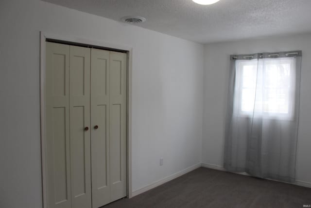 unfurnished bedroom featuring a textured ceiling, dark carpet, and a closet