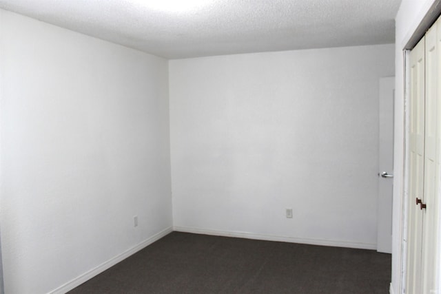 empty room with dark carpet and a textured ceiling