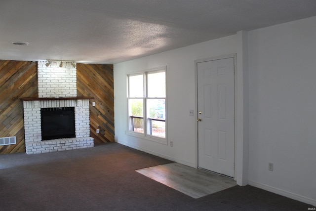 unfurnished living room featuring wooden walls, dark carpet, a textured ceiling, and a brick fireplace