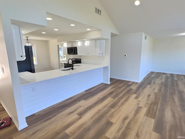 kitchen with kitchen peninsula, white cabinets, hardwood / wood-style flooring, vaulted ceiling, and sink