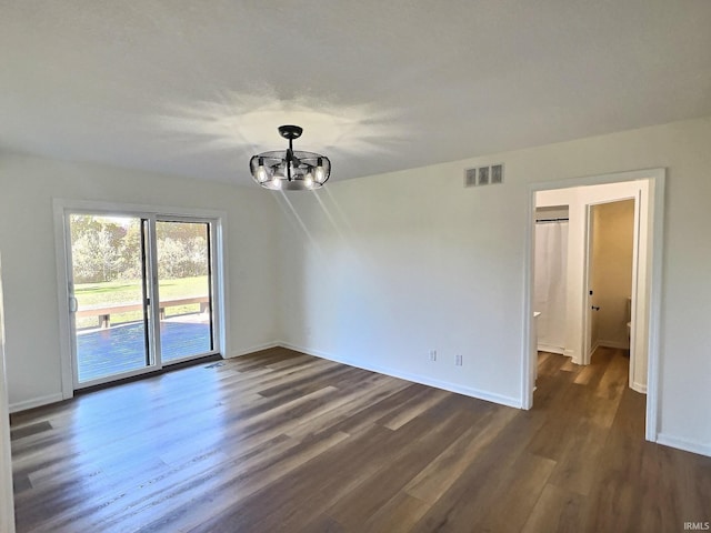 empty room with a notable chandelier and dark hardwood / wood-style flooring