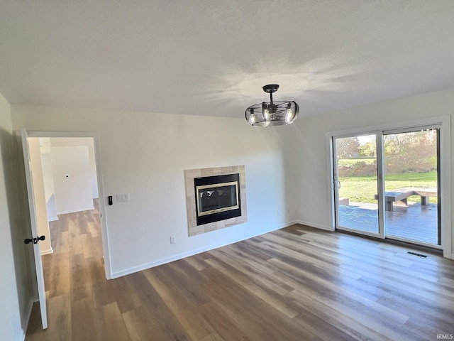 unfurnished living room featuring hardwood / wood-style floors, a tiled fireplace, and vaulted ceiling