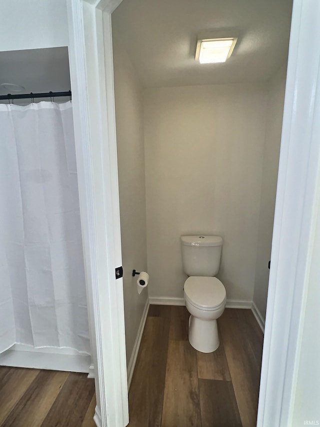 bathroom featuring curtained shower, wood-type flooring, and toilet