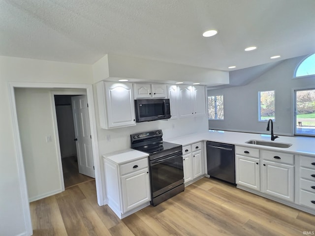 kitchen with sink, black appliances, white cabinetry, and light wood-type flooring