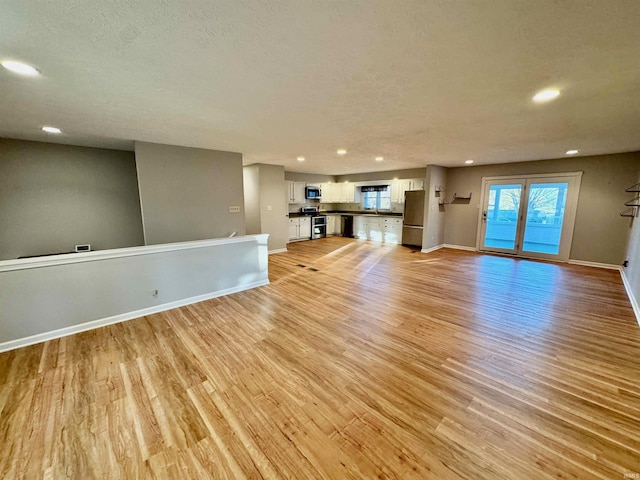 unfurnished living room with recessed lighting, baseboards, a textured ceiling, and light wood-style floors
