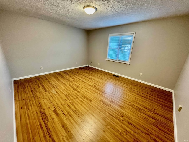 spare room with baseboards, a textured ceiling, wood finished floors, and visible vents