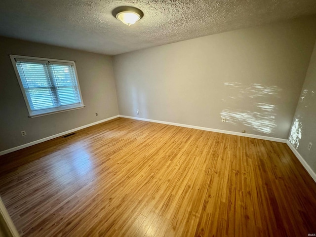 spare room with visible vents, a textured ceiling, baseboards, and wood finished floors