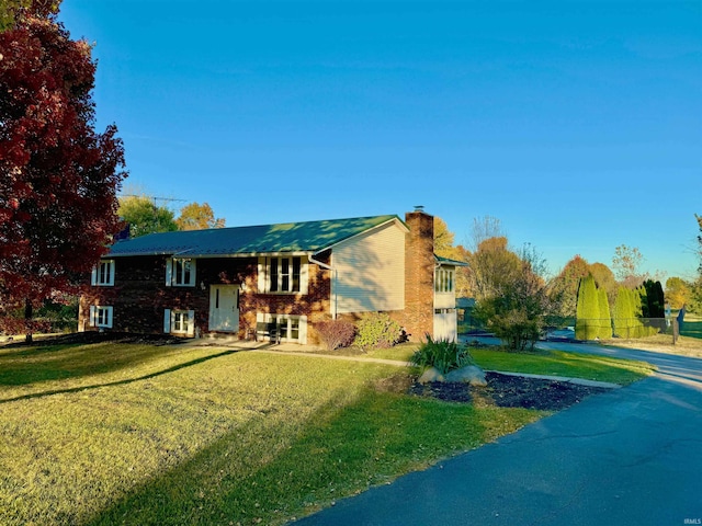 bi-level home featuring a chimney, brick siding, and a front yard