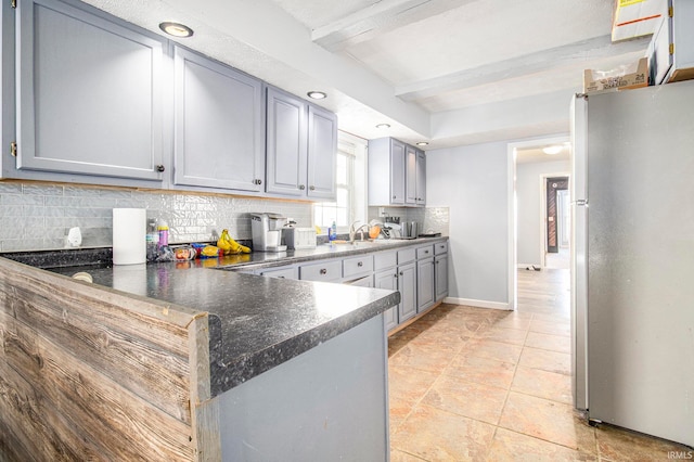 kitchen with kitchen peninsula, tasteful backsplash, stainless steel refrigerator, beamed ceiling, and gray cabinets