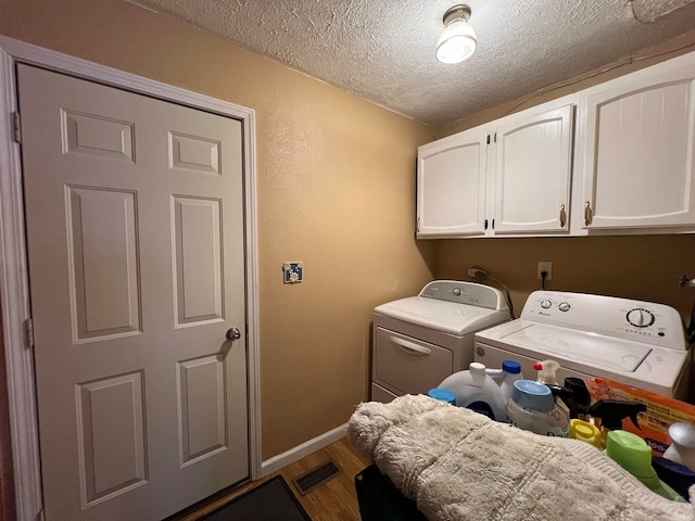 washroom featuring wood-type flooring, a textured ceiling, cabinets, and washing machine and clothes dryer