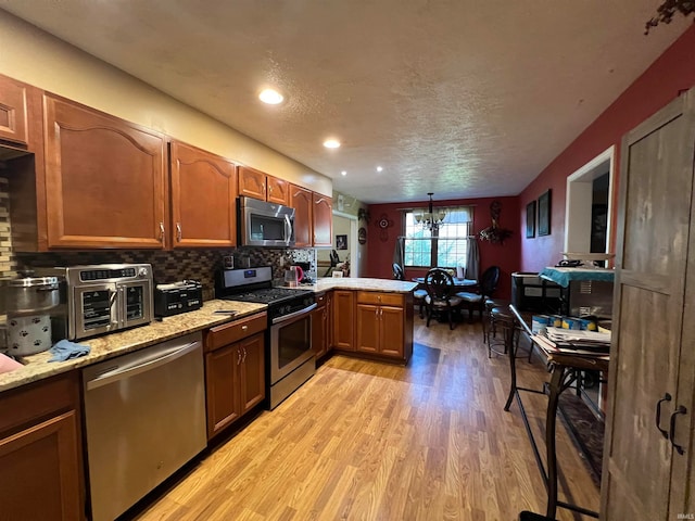 kitchen featuring appliances with stainless steel finishes, a textured ceiling, kitchen peninsula, light hardwood / wood-style flooring, and a chandelier