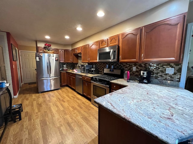 kitchen featuring decorative backsplash, kitchen peninsula, stainless steel appliances, light stone counters, and light hardwood / wood-style floors