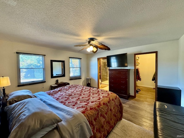 bedroom with ceiling fan, multiple windows, a walk in closet, and hardwood / wood-style floors