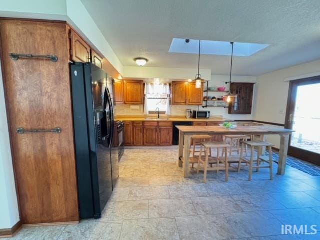 kitchen with sink, pendant lighting, black refrigerator with ice dispenser, and a skylight