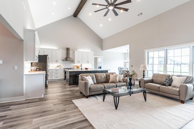 living room with beam ceiling, sink, light wood-type flooring, high vaulted ceiling, and ceiling fan