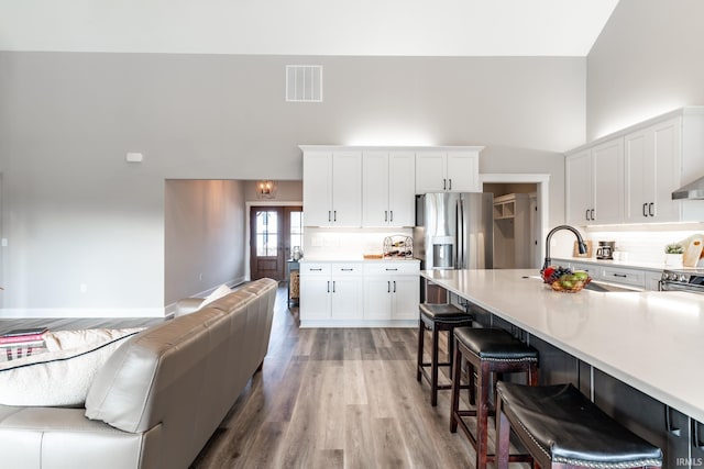 kitchen with a high ceiling, hardwood / wood-style floors, white cabinets, a kitchen bar, and appliances with stainless steel finishes