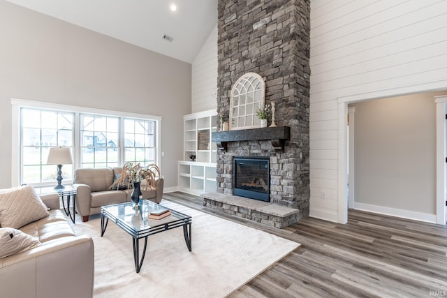 living room featuring high vaulted ceiling, wood-type flooring, and a stone fireplace