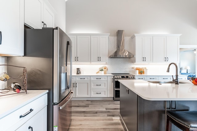 kitchen with wall chimney exhaust hood, appliances with stainless steel finishes, light hardwood / wood-style floors, and white cabinets