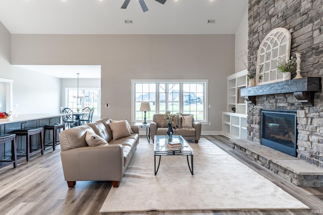 living room featuring ceiling fan with notable chandelier, wood-type flooring, plenty of natural light, and a fireplace